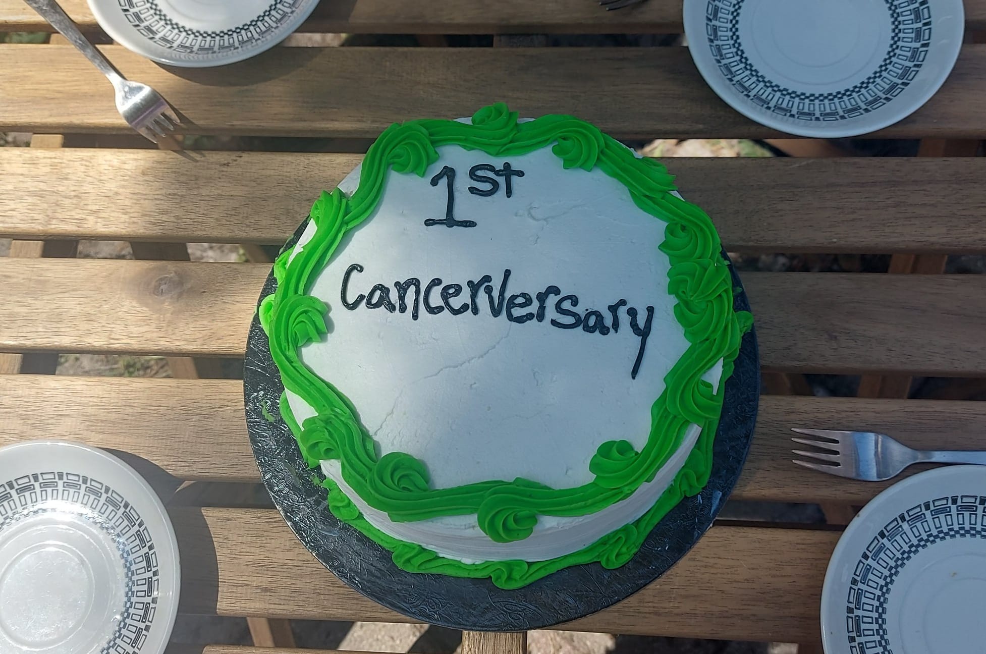 A cake with white icing and green decoration, the text "1st Cancerversary" has been written on it